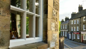 The image showcases a picturesque European street lined with historic buildings with thin double glass in Georgia each displaying unique architectural features such as ornate balconies stone faades and wooden structures In the foreground a traditional window with a classic sash frame