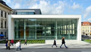 The image showcases a modern architectural design featuring large sleek windows that highlight the use of Land Vac vacuum glazing The building is set against a backdrop of a vibrant Polish city with historical structures nearby that contrast with the surroundings